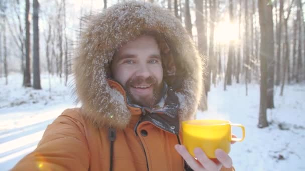 Kış turizmi ve yürüyüş konsepti. Genç sakallı adam ormanda bir kupa sıcak çayla selfie çekiyor. - Video, Çekim
