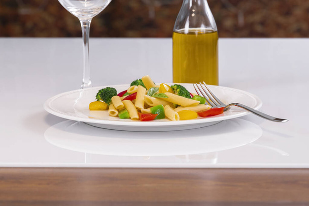 Selective focus of a plate with pasta salad and a fork, with an out of focus bottle of oil at the back. Pasta and healthy food concept. - Valokuva, kuva