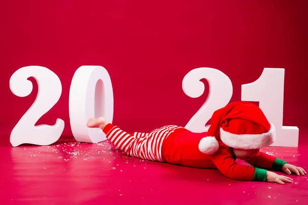 little boy lying on studio floor in santa costume with 2021 numbers - Photo, Image