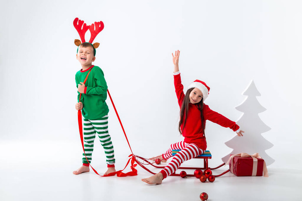 Junge mit Hirschhörnern trägt Mädchen mit Weihnachtsmütze auf Schlitten - Foto, Bild
