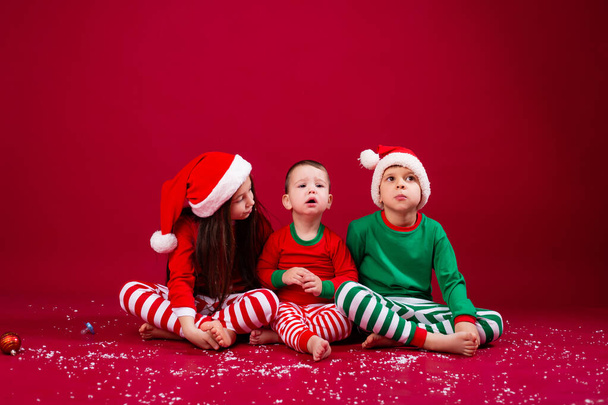 girl looking at brothers, kids in festive costumes sitting on studio floor - Foto, afbeelding