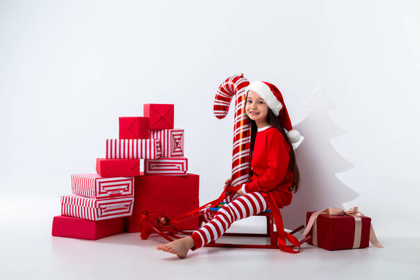 little girl posing with candy cane balloon and many gifts sitting on sleigh - Photo, image