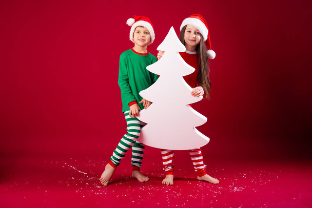 αδελφός και αδελφή σε εορταστικές στολές κρατώντας χριστουγεννιάτικο δέντρο σε σχήμα διακόσμησης - Φωτογραφία, εικόνα