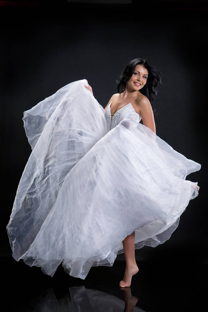Young beautiful barefooted woman in a wedding dress on a black background - Foto, Imagem