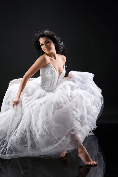 Young beautiful barefooted woman in a wedding dress on a black background - Фото, изображение
