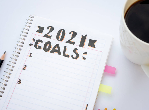 Decorated striped notebook for writing New Year's resolutions with colored dividers on the sides on a white table and a black coffee cup on the side in close up concept. - Photo, Image