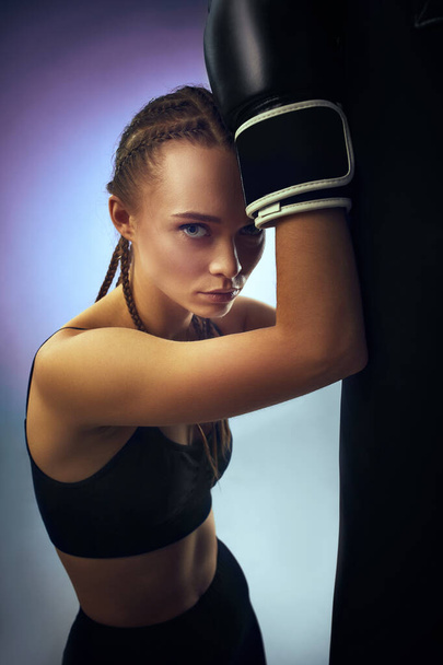 athletic woman in black boxing gloves leaning on punching bag - Φωτογραφία, εικόνα
