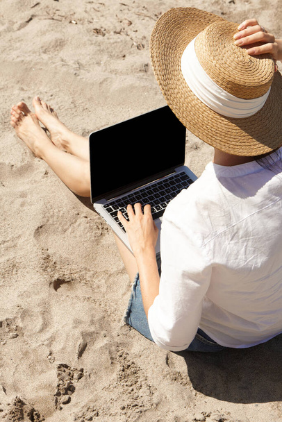 Νεαρή γυναίκα χρησιμοποιεί φορητό υπολογιστή σε μια παραλία. Επικοινωνία τρόπου ζωής διακοπών. Έννοια της ελεύθερης εργασίας - Φωτογραφία, εικόνα