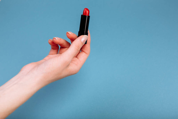 The woman's hand is taking red lipstick. isolated On the blue background. - 写真・画像