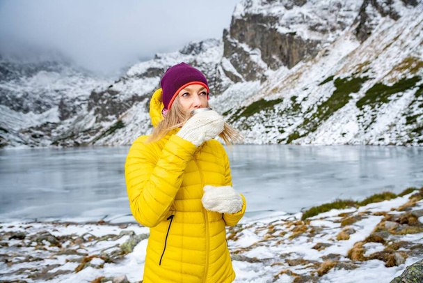 A cold woman tourist is drinking hot tea in a beautiful mountain landscape. - Fotografie, Obrázek