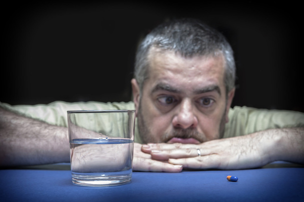 Frustrierter junger Mann sitzt am Tisch und schaut auf die Pille - Foto, Bild
