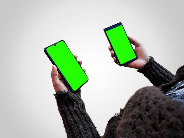 θηλυκό κρατώντας δύο έξυπνα τηλέφωνα mock up στα χέρια με πράσινη οθόνη απομονωμένη - Φωτογραφία, εικόνα
