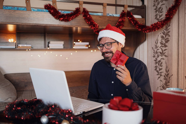 Εικονικό Χριστουγεννιάτικο πάρτι. Άνθρωπος χαμογελώντας φορώντας Σάντα καπέλο Business video conferencing Online ομάδα συνάντηση τηλεδιάσκεψη καλώντας από το σπίτι. - Φωτογραφία, εικόνα