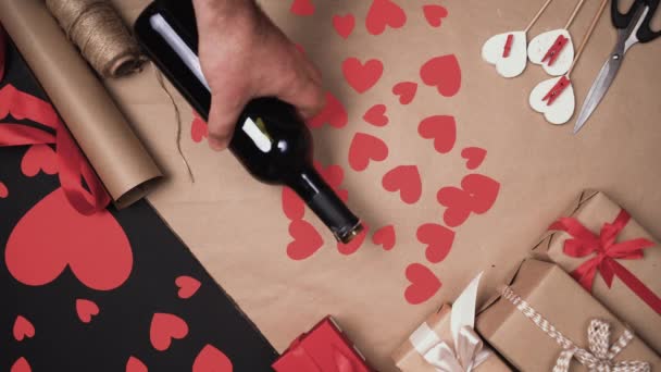 На фоне бумажных сердец руки человека кладут бутылку вина и два бокала. День святого Валентина - Кадры, видео