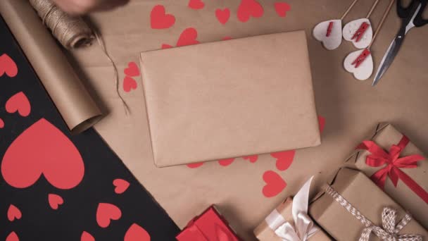 manos masculinas poner una caja envuelta en papel artesanal y empezar a envolverlo con cinta adhesiva. Concepto de regalos de San Valentín - Metraje, vídeo