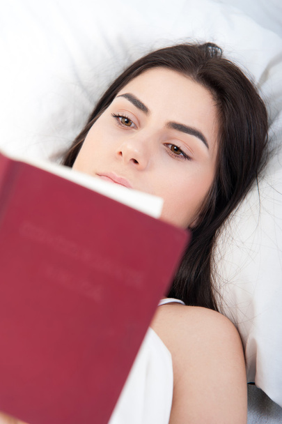 Расслабляющая молодая красивая женщина читает в постели
 - Фото, изображение