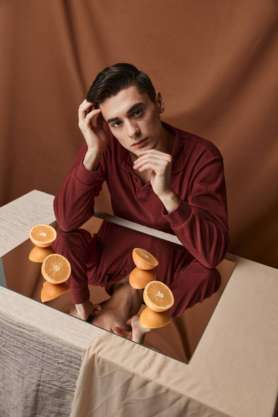 Chlápek u stolu se zrcadlem a řezané pomeranče košile hnědé pozadí - Fotografie, Obrázek