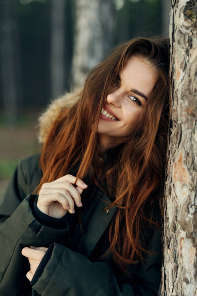 усміхнена жінка тримає волосся ліктями на дереві в природі
 - Фото, зображення