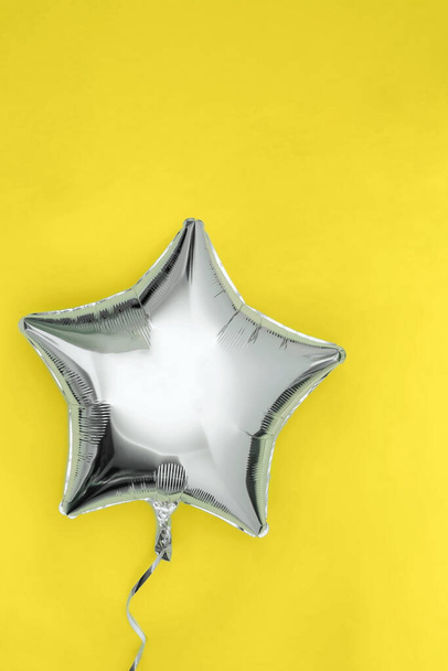Серебряный блестящий шарик в форме звезды в форме фольги, изолированный на ярко-желтом фоне. Иллюминирующие и окончательные серые цвета 2021 года - Фото, изображение