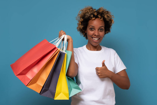 笑顔アフリカの女性でショッピングバッグ表示親指アップジェスチャー. - 写真・画像
