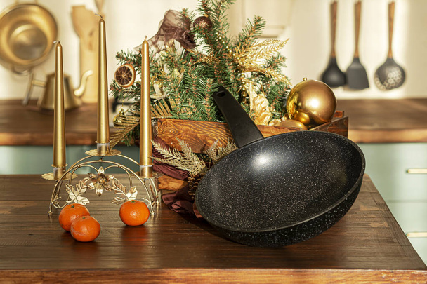 Ceramic frying pan in black, on the rustic kitchen table. Christmas decorations in the background. - Фото, зображення