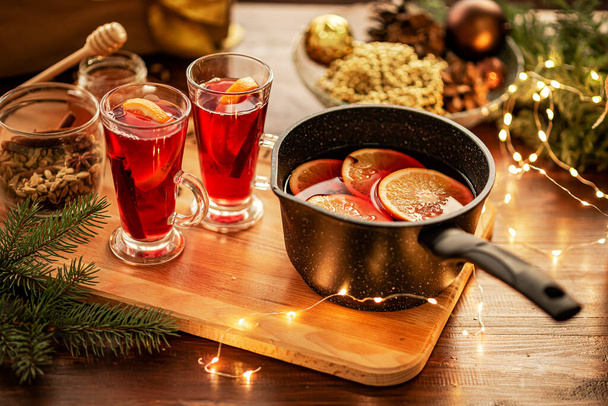 Rode glühwein op tafel, kerstversiering op de achtergrond. Kookproces. - Foto, afbeelding