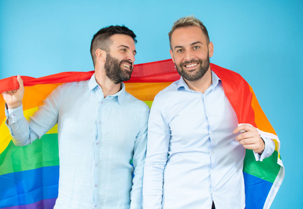 Un jeune couple gay tenant un drapeau sur fond bleu. - Photo, image