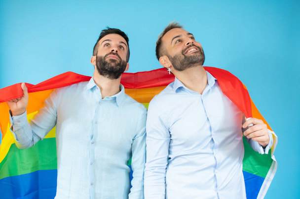 Mladý homosexuální pár drží vlajku nad modrým pozadím. - Fotografie, Obrázek