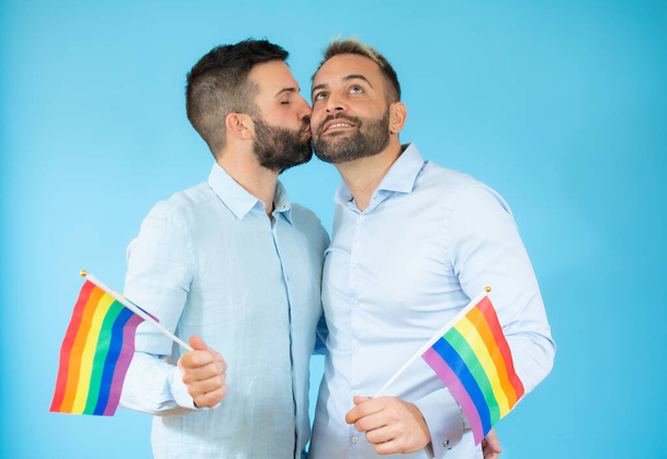 若いゲイのカップルが青い背景に旗を掲げて. - 写真・画像