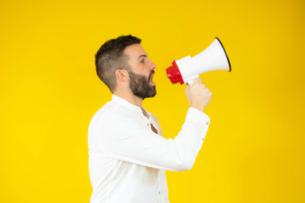 Man yelling into a megaphone over yellow background. - Foto, immagini