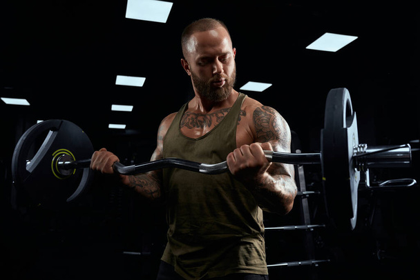 Muscular sportsman building biceps with barbell. - Foto, Bild
