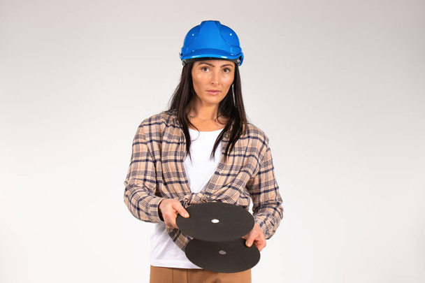 A handywoman in a hard hat holds an abrasive disc for grinder. Female builder. White background. High quality photo - Zdjęcie, obraz
