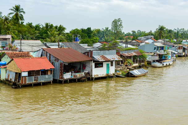 Delta do Mekong no Vietname. Barcos no rio com água castanha. Casas de cidadãos locais na margem do rio. - Foto, Imagem