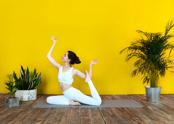 Jovem morena feminina em sportswear branco no tapete e fazendo ioga enquanto pratica mindfulness - Foto, Imagem