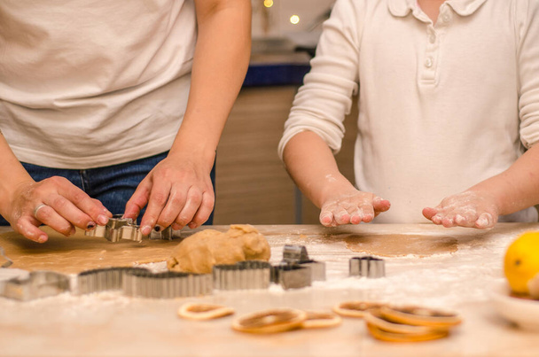 Anne ve kızının elleri Noel için zencefilli kurabiye hazırlıyor, hamuru yuvarlıyor ve kurabiyeleri kurabiye kesiciyle kesiyor. - Fotoğraf, Görsel