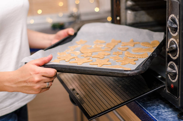 Female hands put a baking sheet with raw ginger Christmas cookies in the oven - Foto, Imagem
