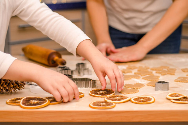 Руки матері і дочки готують святкове імбирне печиво на Різдво, дівчина прикрашає стіл сухими апельсинами
 - Фото, зображення