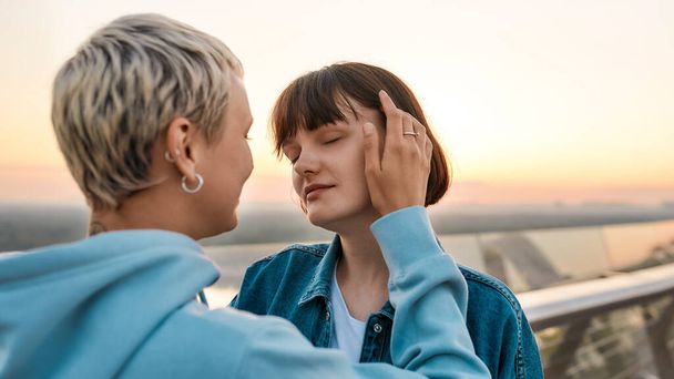 Close up of young sensual lesbian couple enjoying romantic moments while standing on the bridge together at sunrise - Foto, afbeelding