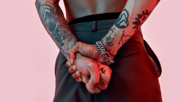 Tattoos showing. A dark-skinned tattooed male standing and holding his hands behind his back turned palms into fists - Photo, image