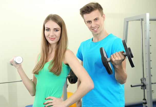 Young beautiful peoples engaged with dumbbells in gym - Zdjęcie, obraz
