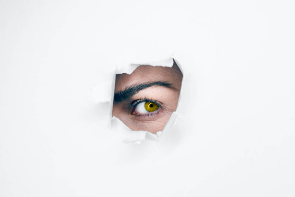 Un occhio femminile giallo sbircia attraverso un buco nero. Combinazioni di colori di tendenza di 2021. - Foto, immagini