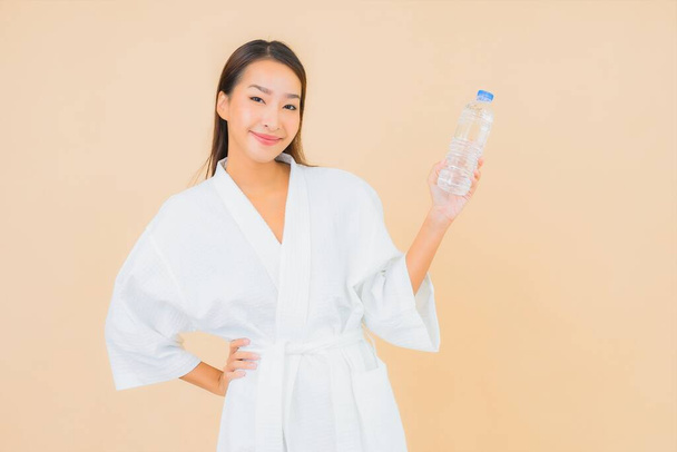 Portrét krásná mladá asijská žena s lahví vody k pití na barevném izolovaném pozadí - Fotografie, Obrázek
