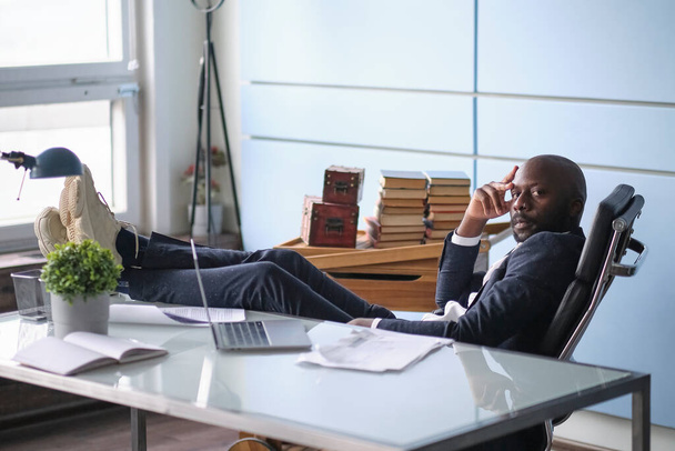 Relaxed worker finished work completed task taking break after hard workday putting head on hand. Thoughtful African American businessman looking out window sitting at office desk. - Foto, imagen