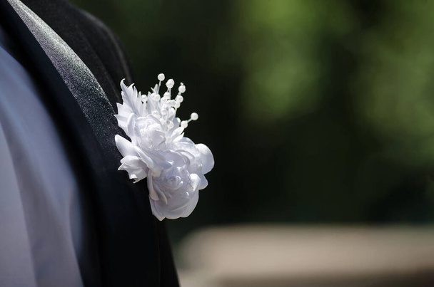 Witte bloem op de zwarte smoking van de bruidegom op een zonnige dag, close-up - Foto, afbeelding