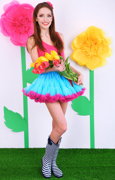Beautiful young woman in petty skirt with bouquet of tulips on decorative background - Foto, afbeelding