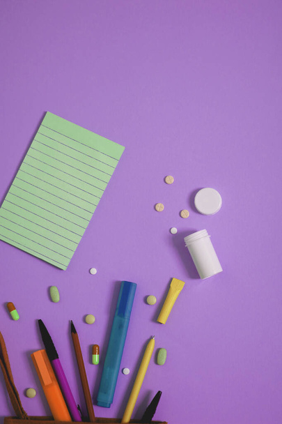 photo urbaine colorée de stylos, marqueurs, bouteille ouverte de médicaments et bloc-notes sur fond violet vif avec espace de copie - Photo, image