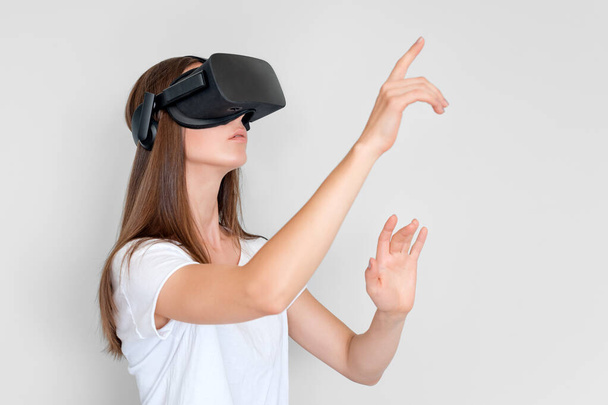 Young woman wearing virtual reality goggles headset, vr box. Connection, technology, new generation, progress concept. Girl trying to touch objects in virtual reality. Studio shot on gray. - Photo, image
