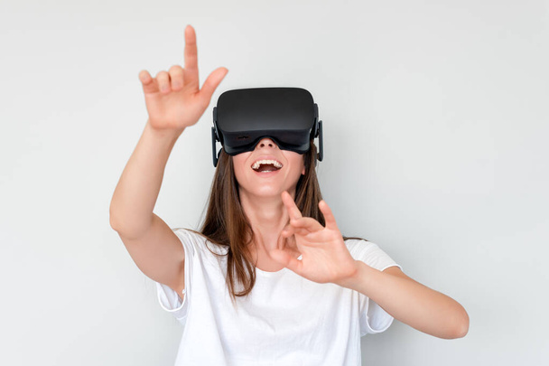 Smiling positive woman wearing virtual reality goggles headset, vr box. Connection, technology, new generation, progress concept. Girl trying to touch objects in virtual reality. Studio shot on gray. - Photo, Image