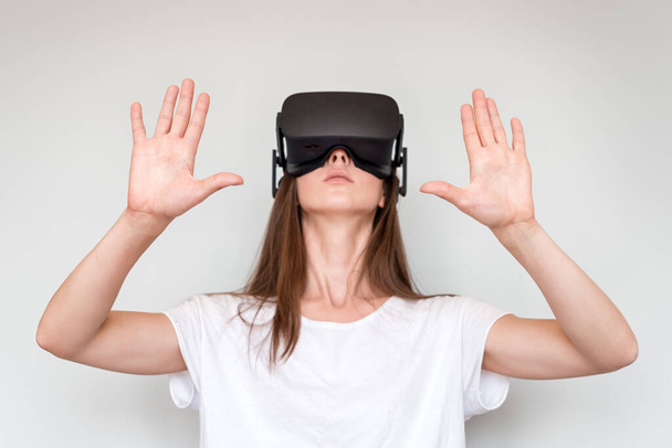 Jonge vrouw met een virtual reality bril op. Verbinding, technologie, nieuwe generatie, vooruitgangsconcept. Meisje probeert objecten aan te raken in virtual reality. Studio shot op grijs. - Foto, afbeelding