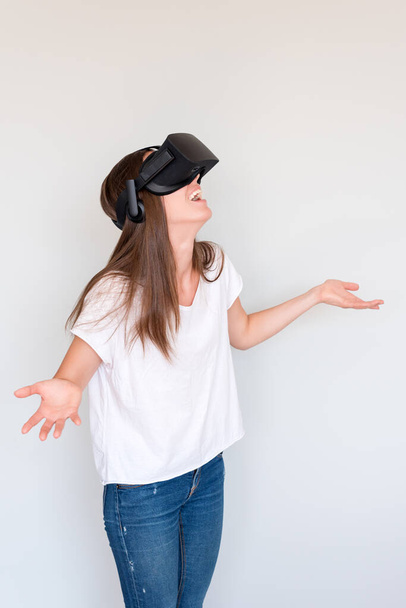Mujer positiva asombrada vistiendo gafas de realidad virtual auriculares, caja vr. Conexión, tecnología, nueva generación, concepto de progreso. Chica sorprendida por algo en la realidad virtual. Estudio filmado en gris. - Foto, imagen